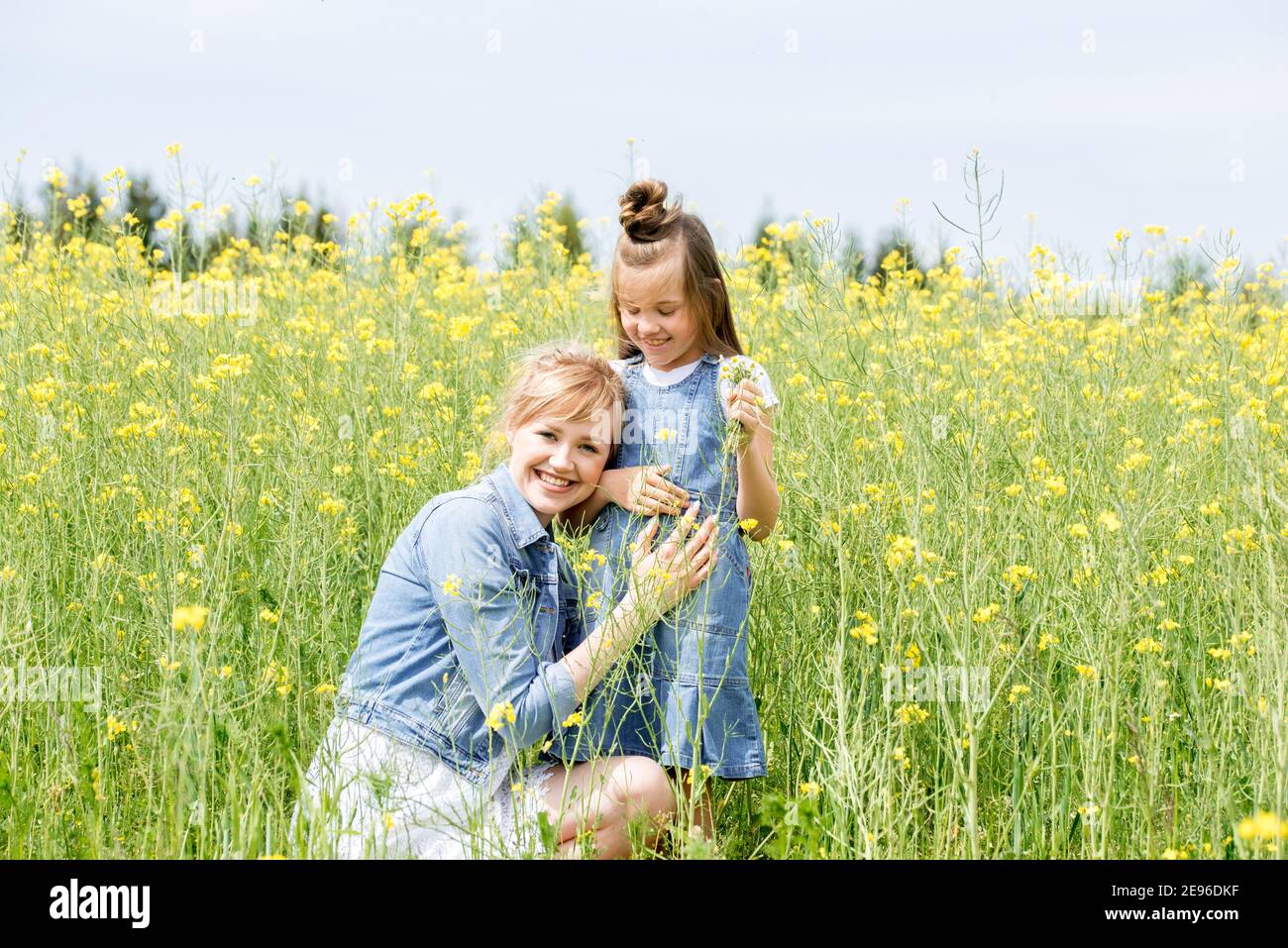 Famiglia felice su un prato estivo. Bambina piccola figlia hugging e baciare madre.Yellow campo di fiori di colza. La libertà è un'idea da sogno. Foto Stock