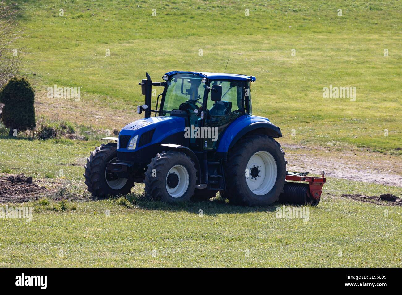 trattore blu pronto per il lavoro sul campo ma senza conducente su un prato verde, fotografato dal lato anteriore, di giorno senza persone Foto Stock