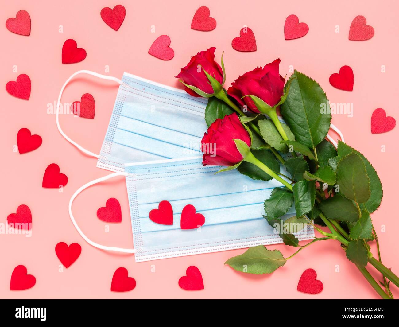 Rose rosse e maschera medica monouso con molti cuori rossi su sfondo rosa. Festa delle madri, delle donne o dei San Valentino nel Coronavirus pande Foto Stock