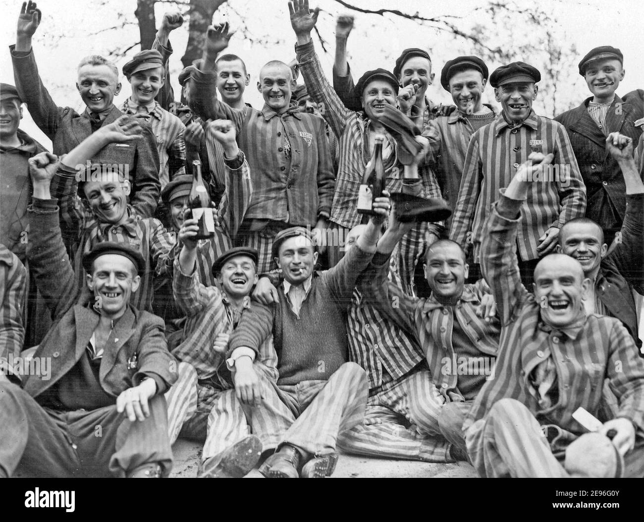 I prigionieri polacchi nel campo di concentramento nazista di Dachau in Germania celebrano con gioia la loro liberazione da parte dell'esercito degli Stati Uniti. L'uomo in piedi al centro tra le bottiglie indossa un triangolo P, aprile 1945 Foto Stock