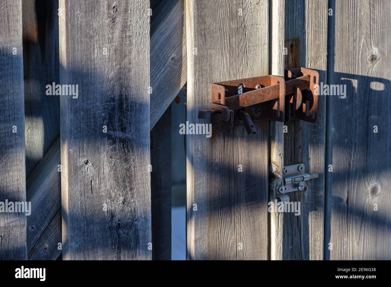 Un dispositivo di chiusura in metallo arrugginito mantiene chiuso il cancello di una recinzione in legno. Foto Stock