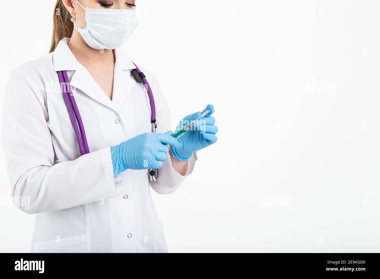 Un giovane infermiere in una maschera apre una siringa su sfondo bianco in un cappotto bianco, per fare una vaccinazione, un'iniezione. Il concetto di vaccinazione e. Foto Stock