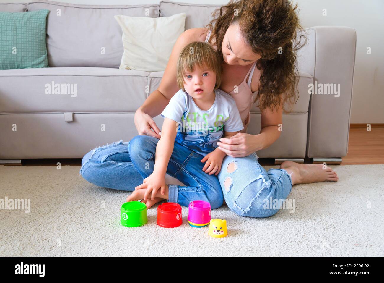 Una sola giovane madre e il suo bambino autentico disabile, giocando nel loro soggiorno Foto Stock