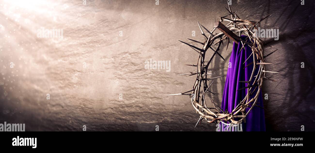 Corona di spine e viola Robe Hanging su Nail in Muro di pietra con raggi di luce - Crocifissione di Gesù Cristo Foto Stock