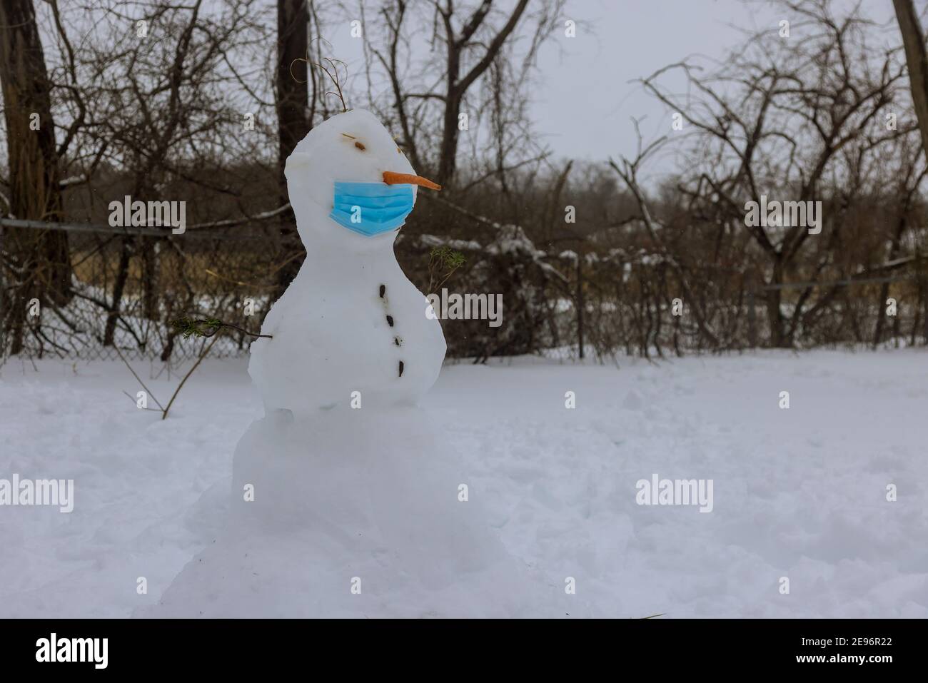 Pupazzo di neve divertente con maschera medica che indossa un durante il coronavirus COVID-19 in un parco innevato sulla neve bianca Foto Stock