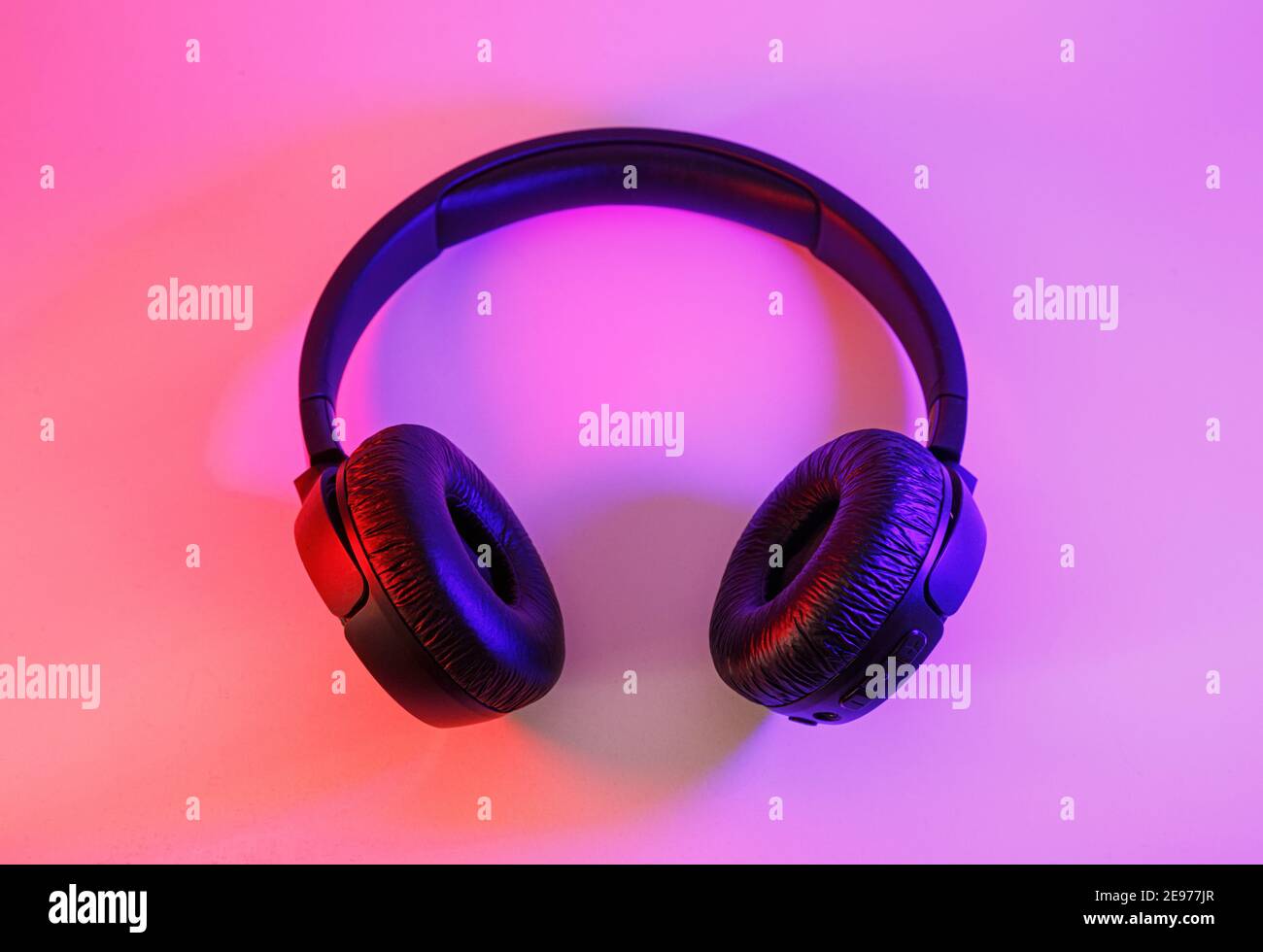 Eleganti cuffie wireless nere illuminate con coloratissima luce al neon su sfondo astratto isolato. Concetto di tecnologia moderna con spazio di copia Foto Stock