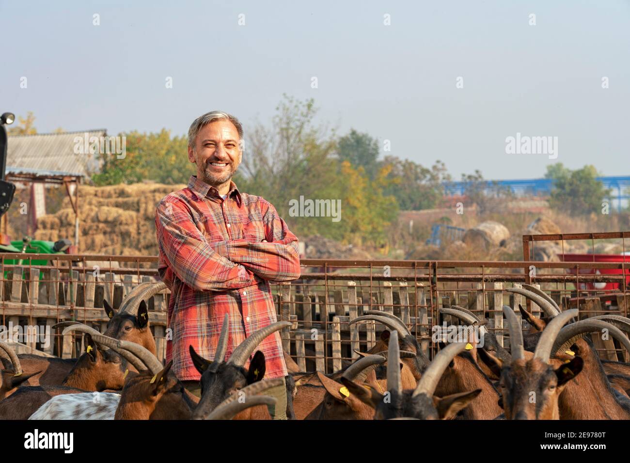 Sorridente contadino maturo in piedi in un recinto di animali all'aperto. Concetto di allevamento animale. Un allevatore alza con attenzione le sue capre a Fattoria animale biologica. Foto Stock