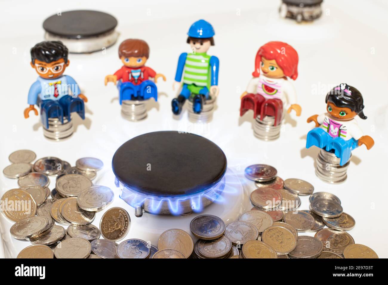 La gente siede vicino al bruciatore di gas sulla stufa e sulle monete di soldi. Il prezzo del gas e delle utenze nel mondo. Foto Stock