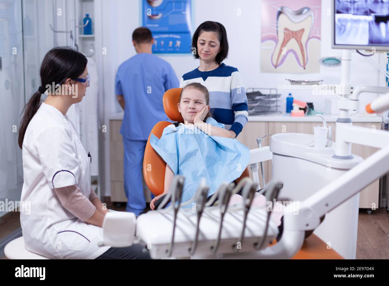 Bambina con espressione dolorosa che mostra dentista dove il suo dente fa male durante il controllo dentale. Bambino con la madre durante il controllo dei denti con stomatolog seduta sulla sedia. Foto Stock