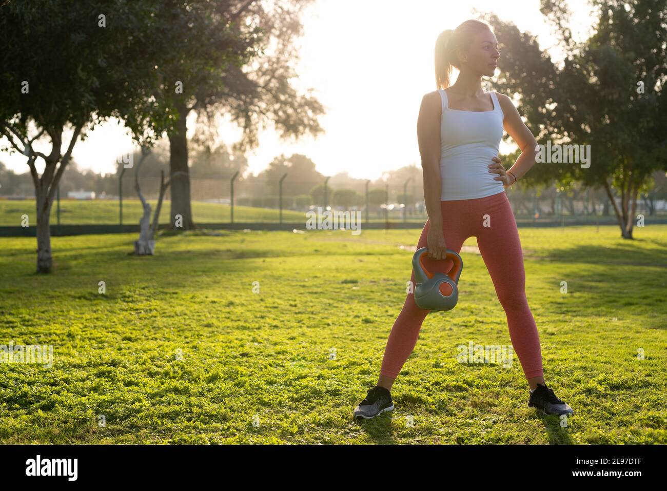 Una giovane donna si impegna in esercizi in mezzo al verde del parco, vestita con pantaloni da yoga rosa e posizionata su un tappetino da yoga. Foto Stock