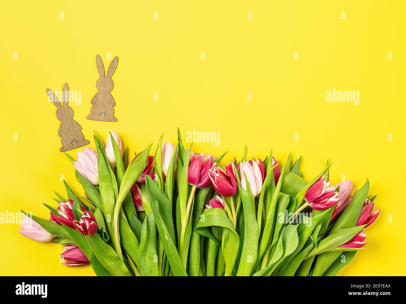 Carta di Pasqua con tulipani rosa e rossi e coniglietto di legno su sfondo giallo. Foto Stock