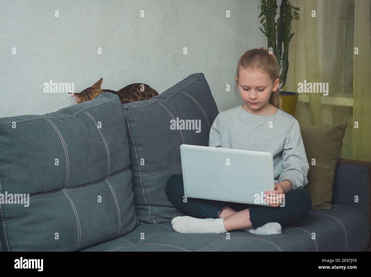 ragazza della scuola seduta sul divano nel soggiorno e tenendo il laptop in grembo, bambini concetto di dipendenza da internet Foto Stock