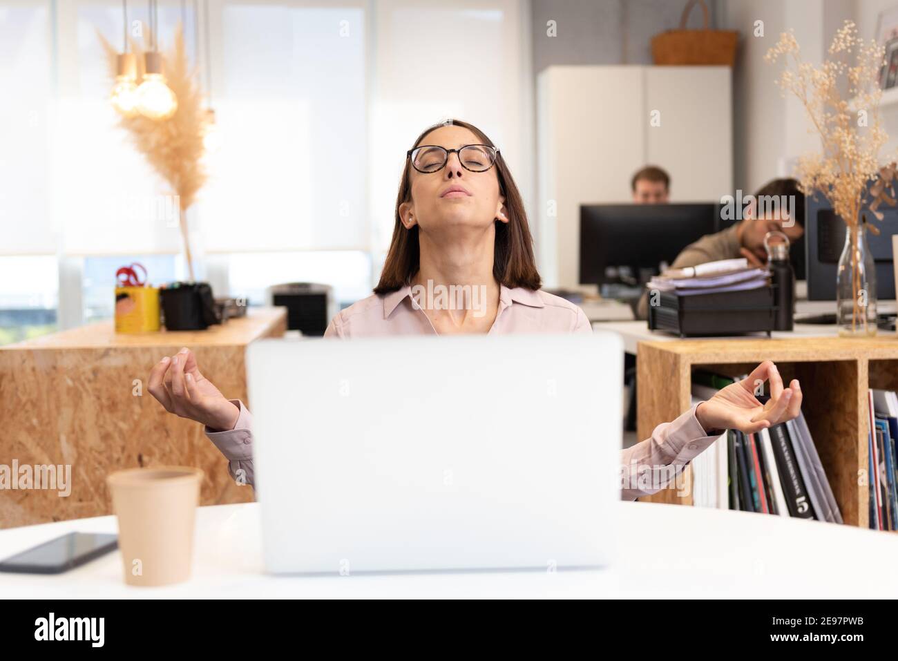 Bella donna ispanica meditando e rilassandosi di fronte al suo portatile in ufficio. Foto Stock