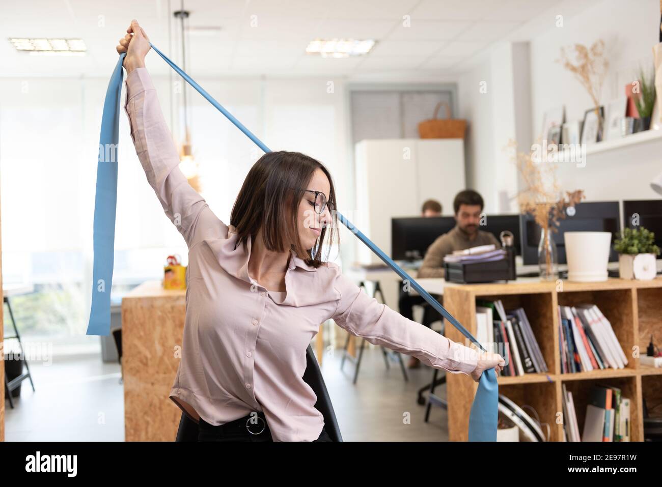 Stile di vita sano nel concetto di luogo di lavoro. Donna ispanica bella stretching con una fascia di gomma pilates in ufficio. Foto Stock