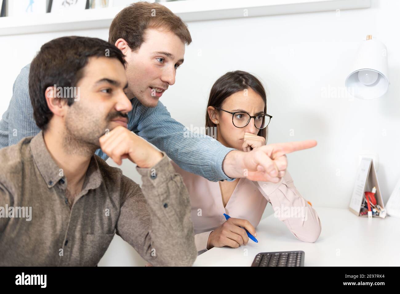 Diversi colleghi che guardano un computer che chiacchiera e contrappone le loro opinioni in ufficio. Foto Stock