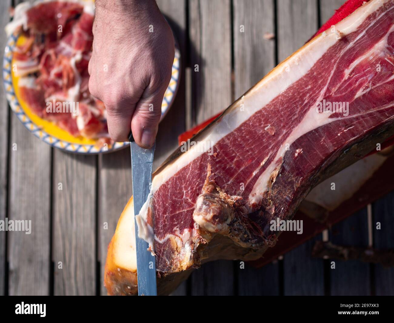 Uomo tagliando una fetta di prosciutto spagnolo secco e piatto con le fette sullo sfondo. Foto Stock
