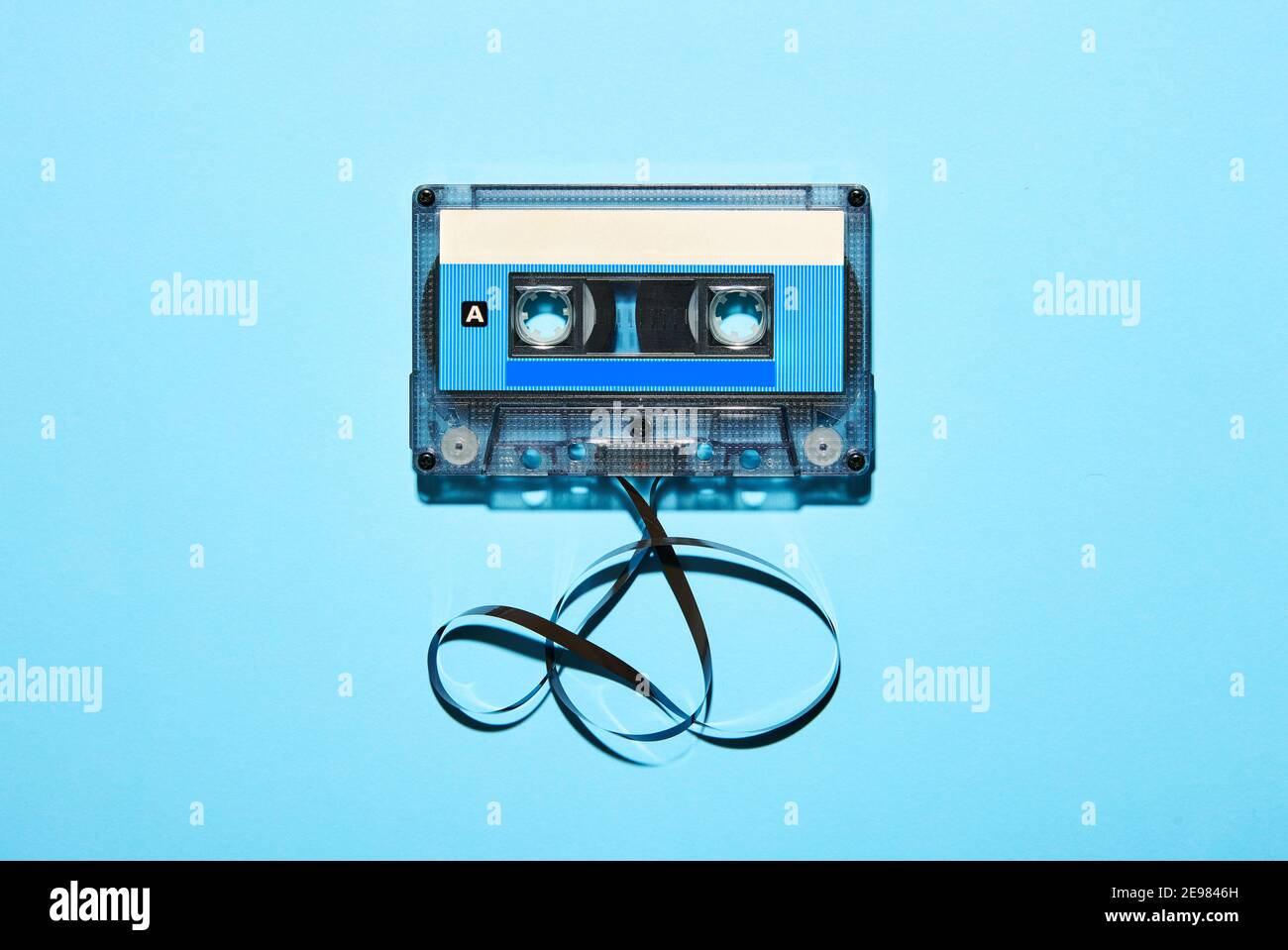 Vista dall'alto della cassetta audio compatta in plastica d'epoca con nastro aggrovigliato isolato su sfondo blu Foto Stock