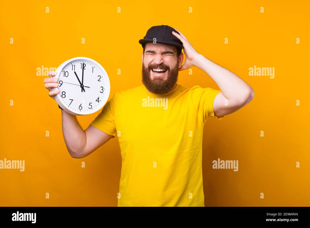 Foto di un giovane uomo bearded che tiene l'orologio da parete e fa un  gesto frustrante, sono in ritardo Foto stock - Alamy