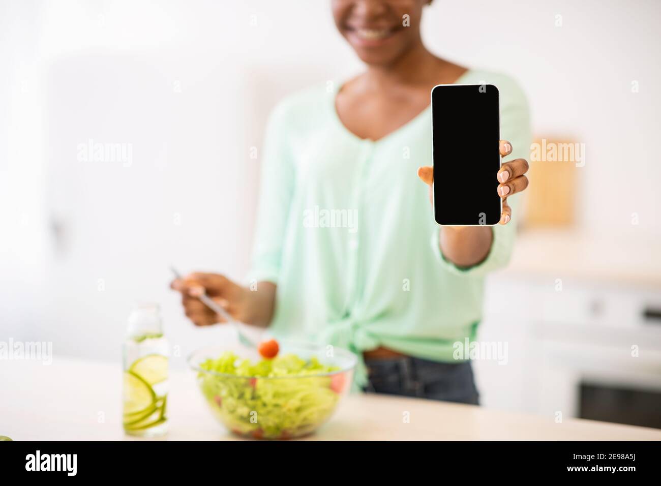 Black Lady che mostra lo schermo del telefono che consiglia l'app Weight-Loss in cucina Foto Stock
