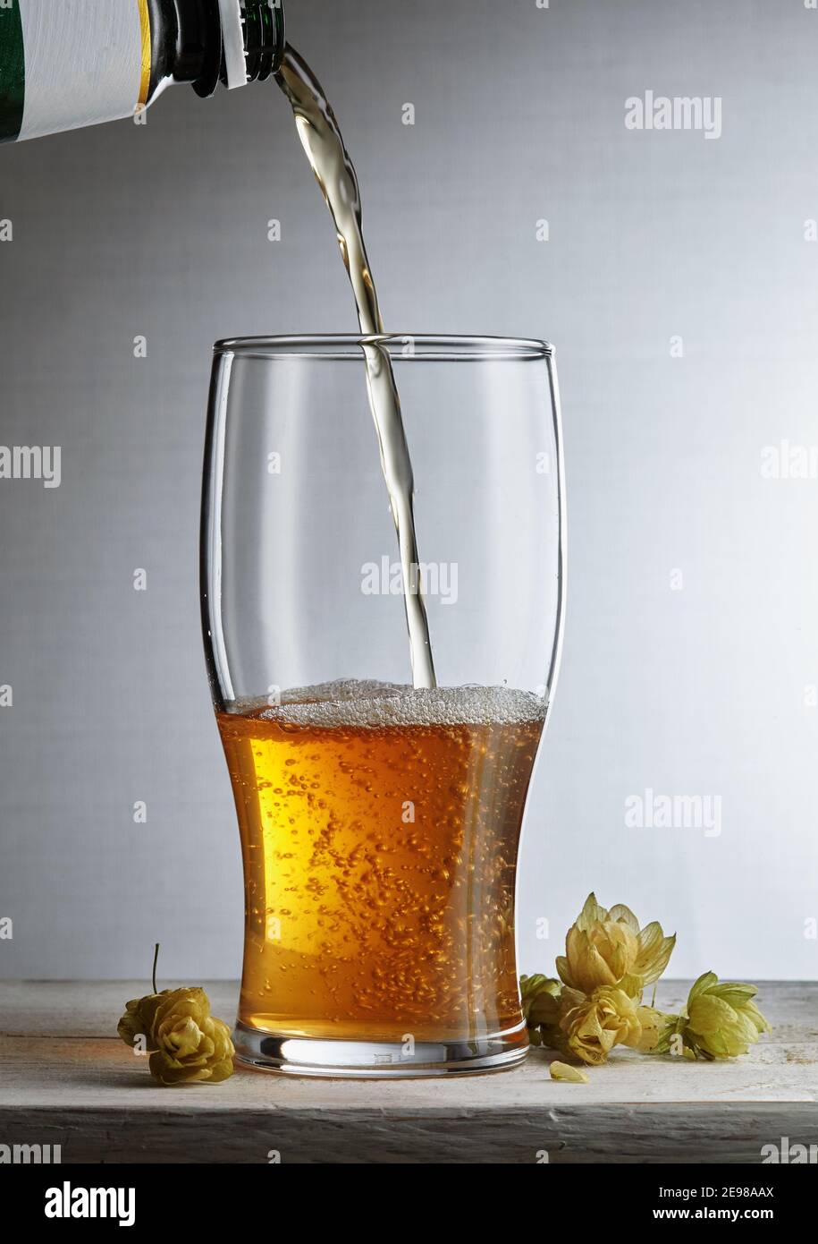 Birra. Birra artigianale leggera e fredda viene versata in un bicchiere. Intorno al luppolo. Primo piano con una pinta di birra Foto Stock