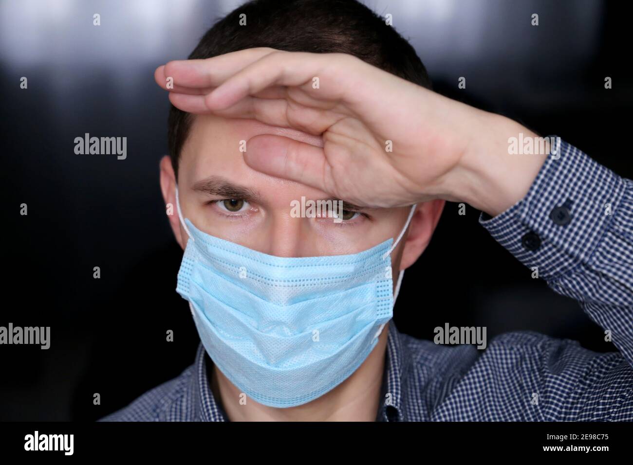 I sintomi del coronavirus e della febbre, l'uomo in maschera di faccia e i vestiti dell'ufficio hanno messo la sua mano sulla fronte. Lavoratore malato, concetto di mal di testa Foto Stock