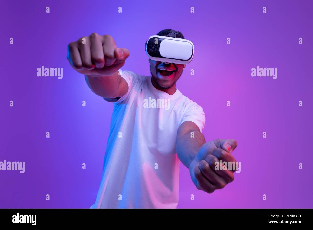 Giovane afroamericano che gioca a videogiochi in VR-occhiali sotto luce viola al neon Foto Stock