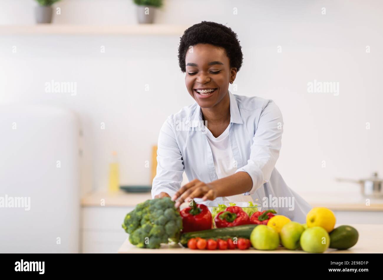 Cheerful African American Lady Cooking Salad per cena in cucina Foto Stock