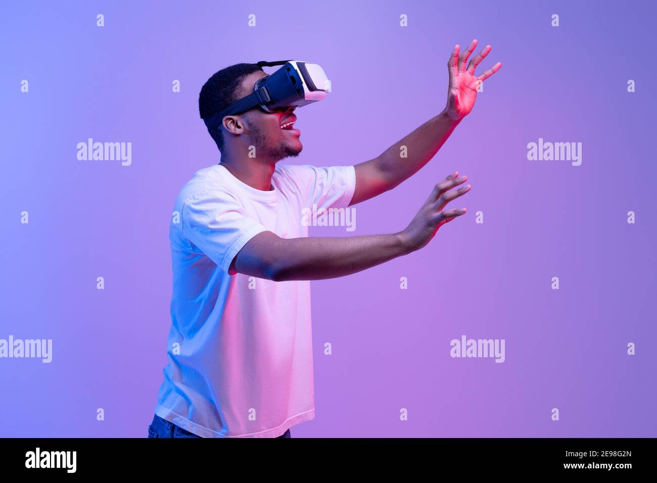 Tecnologia VR. Un ragazzo africano entusiasta che indossa cuffie per realtà virtuale e un vivace sfondo al neon Foto Stock
