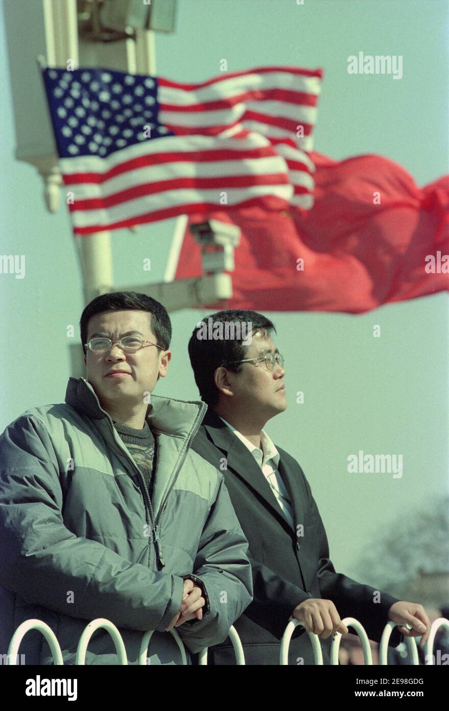 Gli uomini cinesi si trovano di fronte alle bandiere cinesi e americane che sorvolano l'area intorno a Piazza Tiananmen quando George W. Bush visita la Cina. 2002 Foto Stock