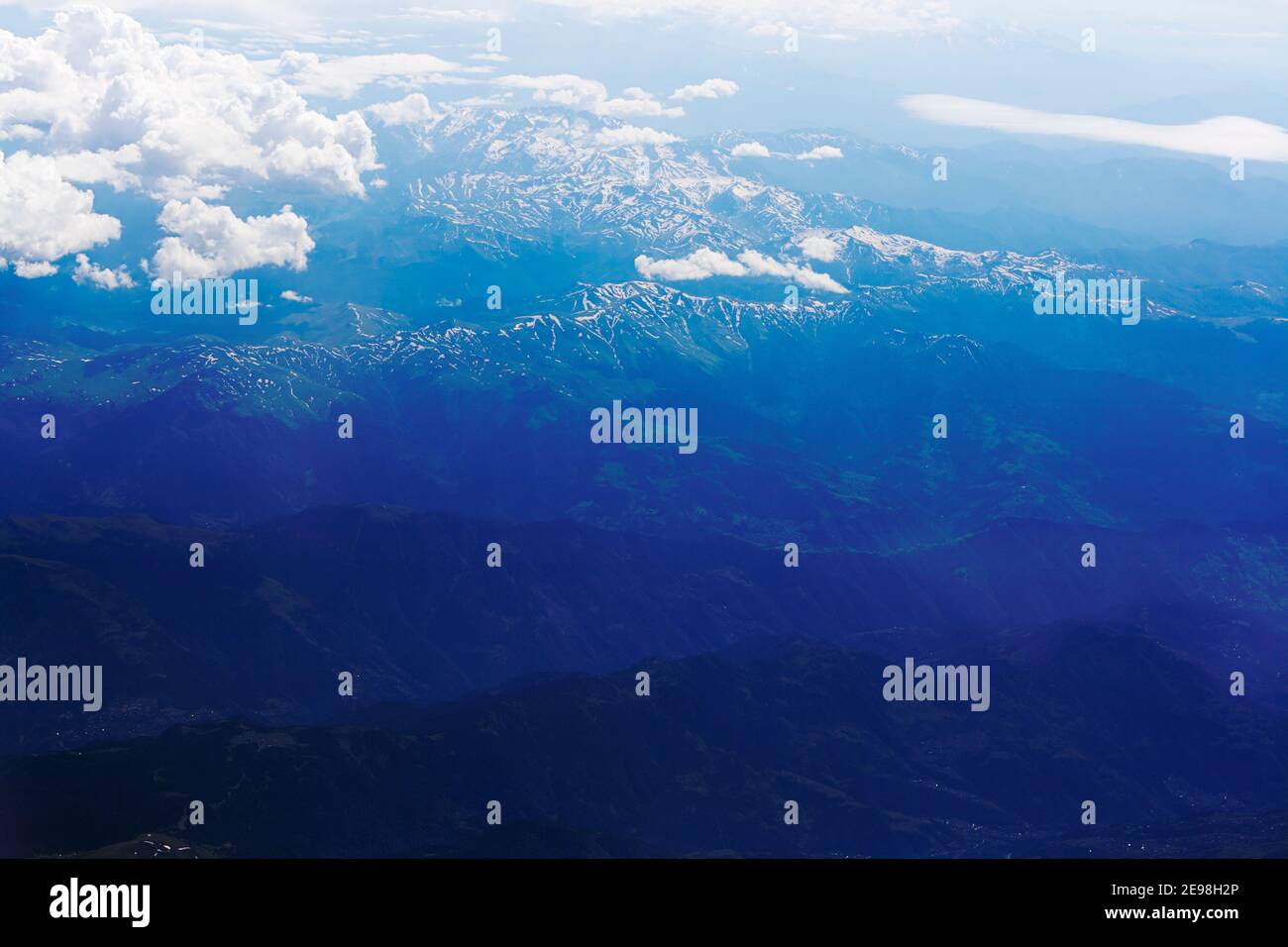 Un cielo blu con nuvole bianche sopra le vette innevate os caucasians vista montagne dalla finestra dell'aereo Foto Stock