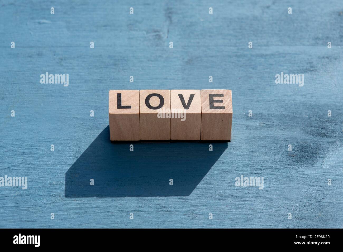 Il concetto di giorno e di emozione felice di Valentin: La parola AMORE scritta con singole lettere cubiche di legno fatte per i giochi da tavolo su superficie testurizzata blu. Foto Stock