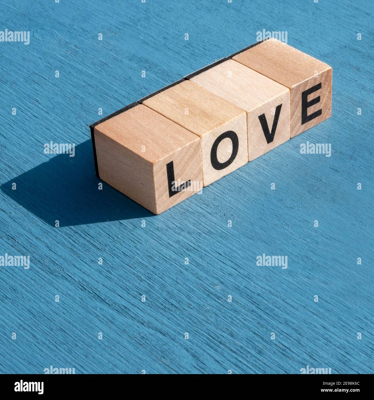 Il concetto di giorno e sensazioni di Valentin: La parola AMORE scritta con lettere cubiche di legno singole per giochi da tavolo su superficie testurizzata blu con spazio Foto Stock