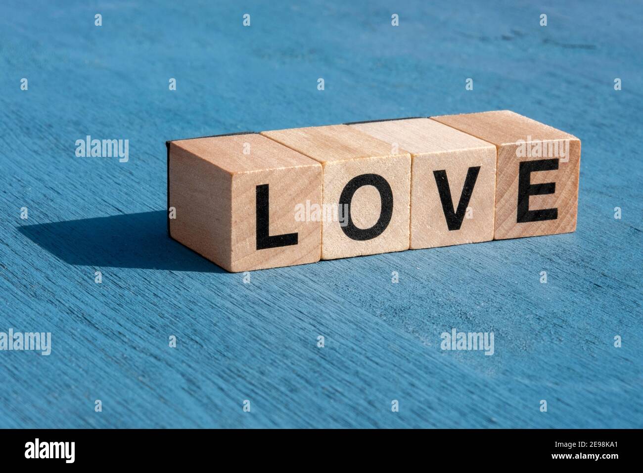 Il concetto di giorno e di emozione felice di Valentin: La parola AMORE scritta con singole lettere cubiche in legno per giochi da tavolo su superficie testurizzata blu con poliziotto Foto Stock