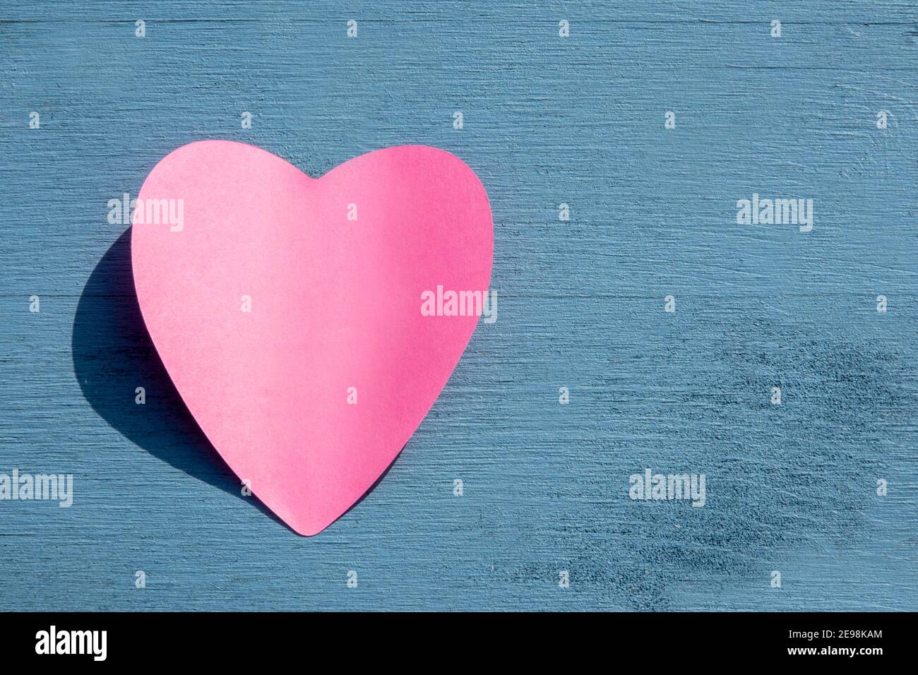Concetto di celebrazione ed evento speciale: Vista dall'alto su un unico adesivo di carta rosa a forma di cuore vuoto su sfondo blu di legno con spazio per la copia. Foto Stock