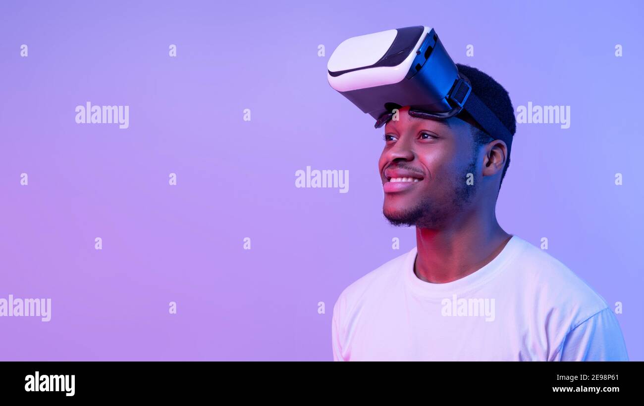 Sorridente afroamericano Guy indossando occhiali VR e guardando da parte, Neon Light Foto Stock