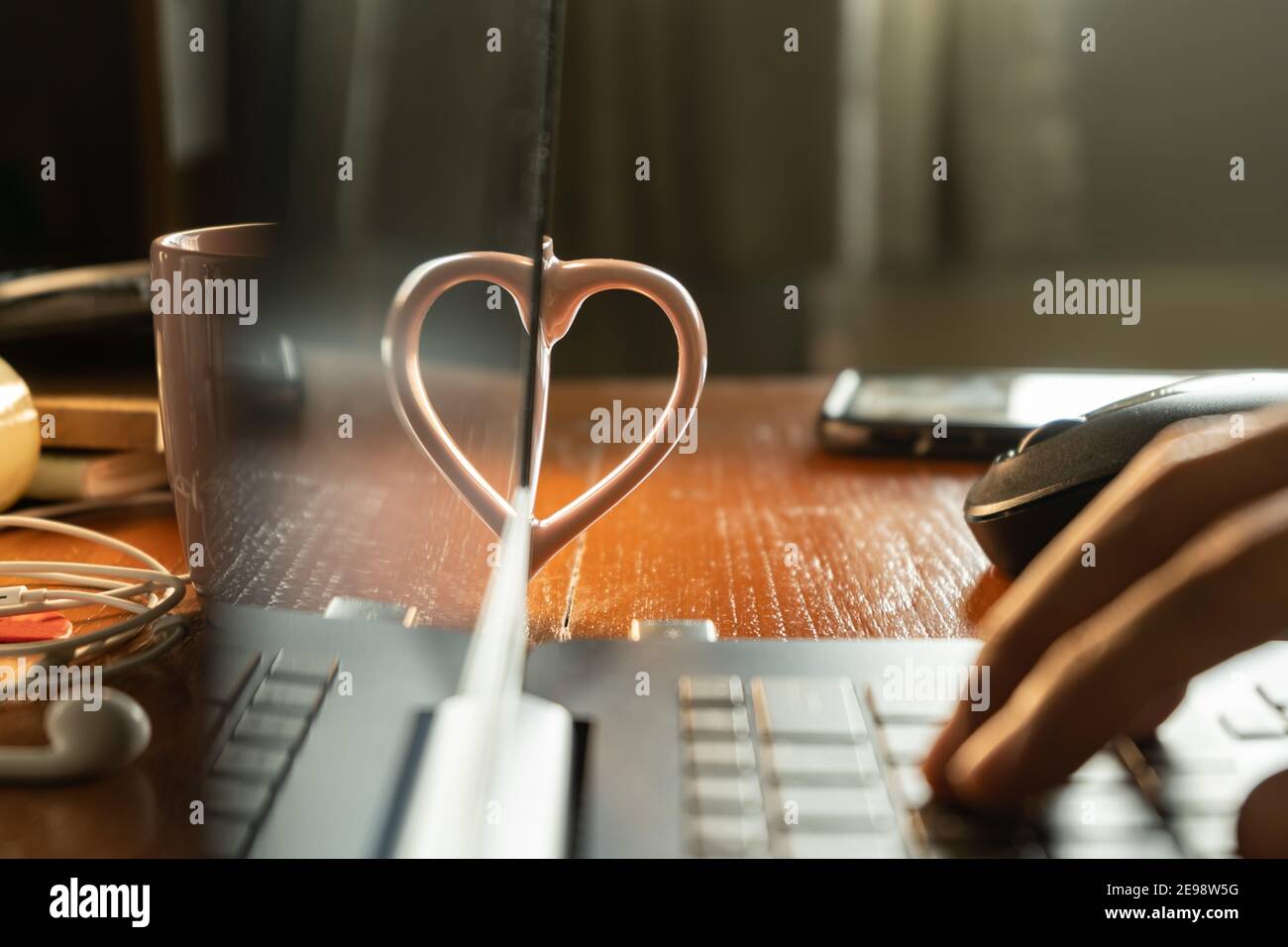 Una forma a cuore realizzata con un manico per tazza e il riflessione dal display del computer portatile Foto Stock