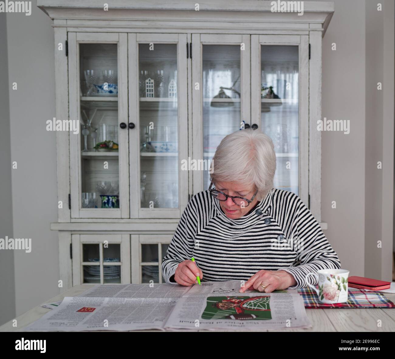 Una donna ha un cuo di caffè al mattino mentre legge la carta e completa un puzzle cruciverba. Foto Stock