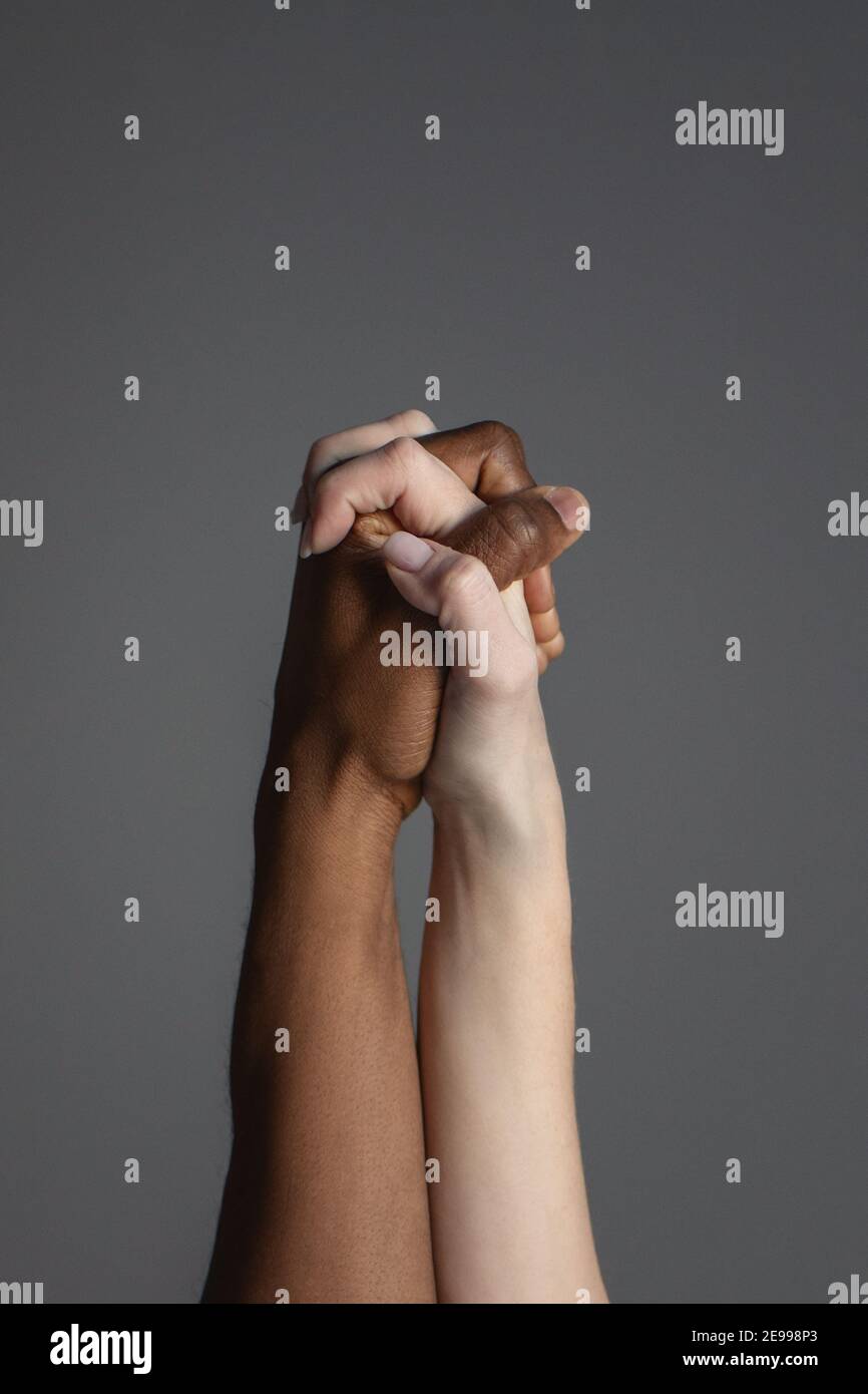 Primo piano di mani bianche e nere di aggrappate insieme su sfondo grigio. Foto Stock