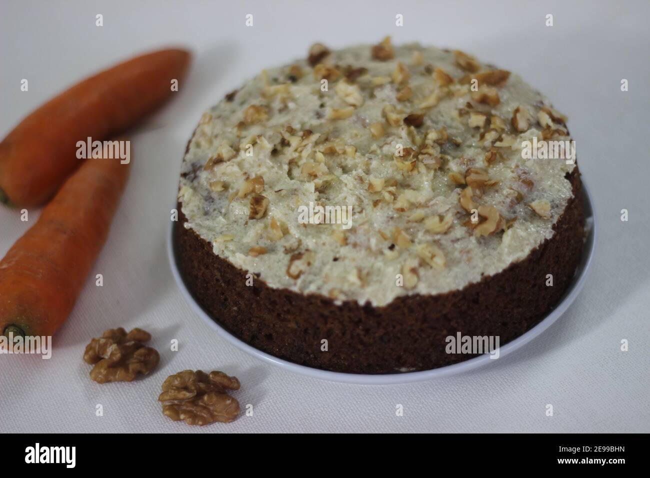 Torta di noce di carota ricoperta da un sottile strato di burro, zucchero e noci tritate. Fotografato con carote su sfondo bianco Foto Stock