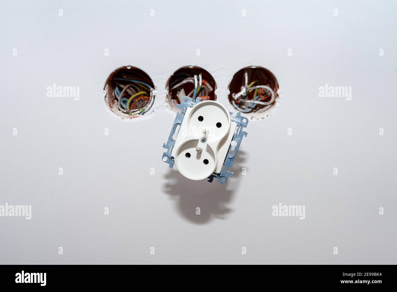Doppia presa elettrica che sporge dalla parete, che si fissa ai cavi elettrici. Foto Stock