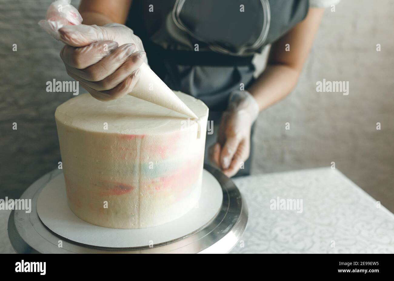 Una ragazza pasticciera fa una torta di nozze con le proprie mani e spreme la crema sugli strati della torta. Un pasticciere produce una crema rosa utilizzando un Foto Stock