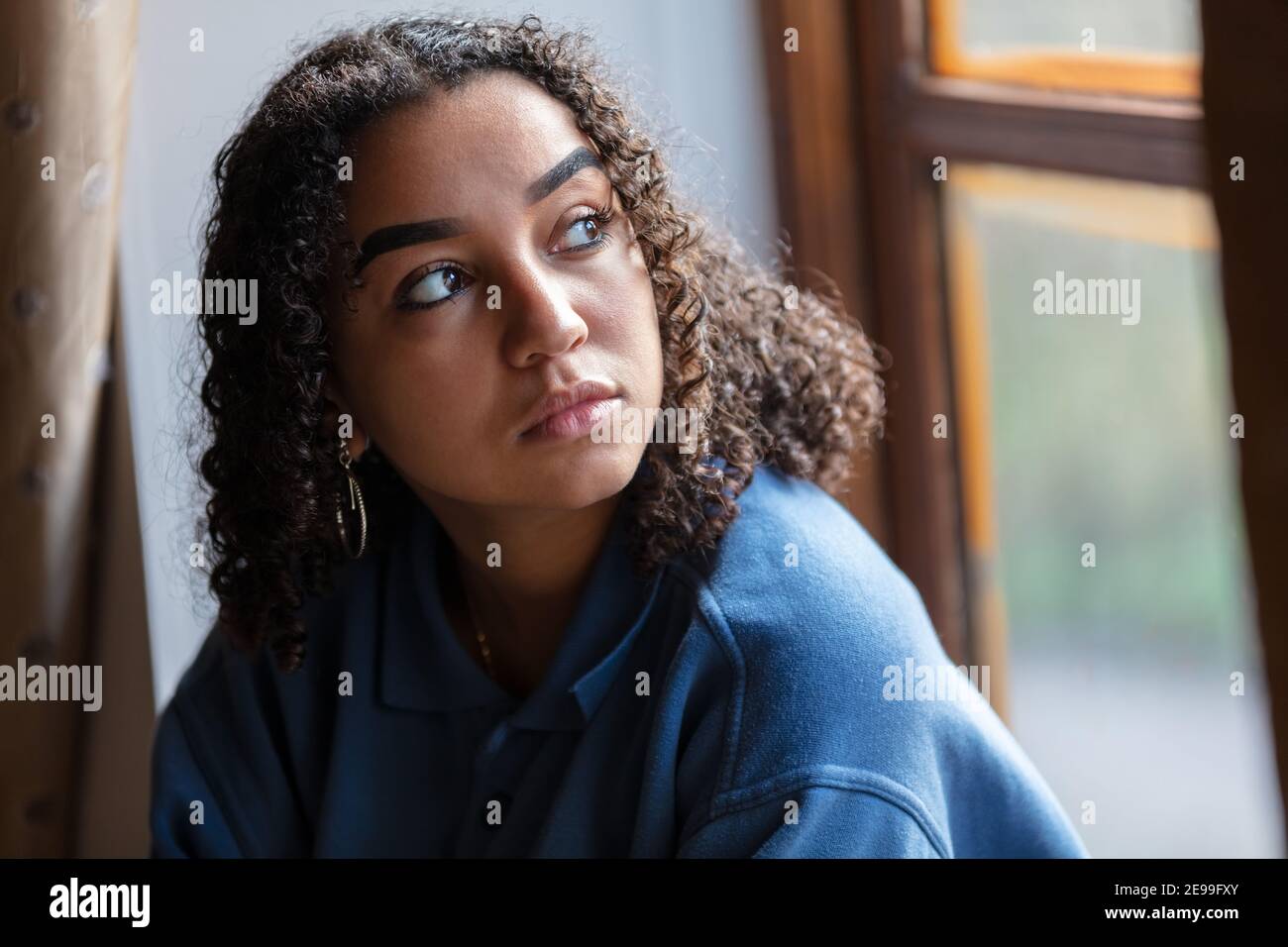 Bella razza mista Africana americana ragazza adolescente femmina giovane donna triste depresso o preoccupato guardando fuori da una finestra Foto Stock