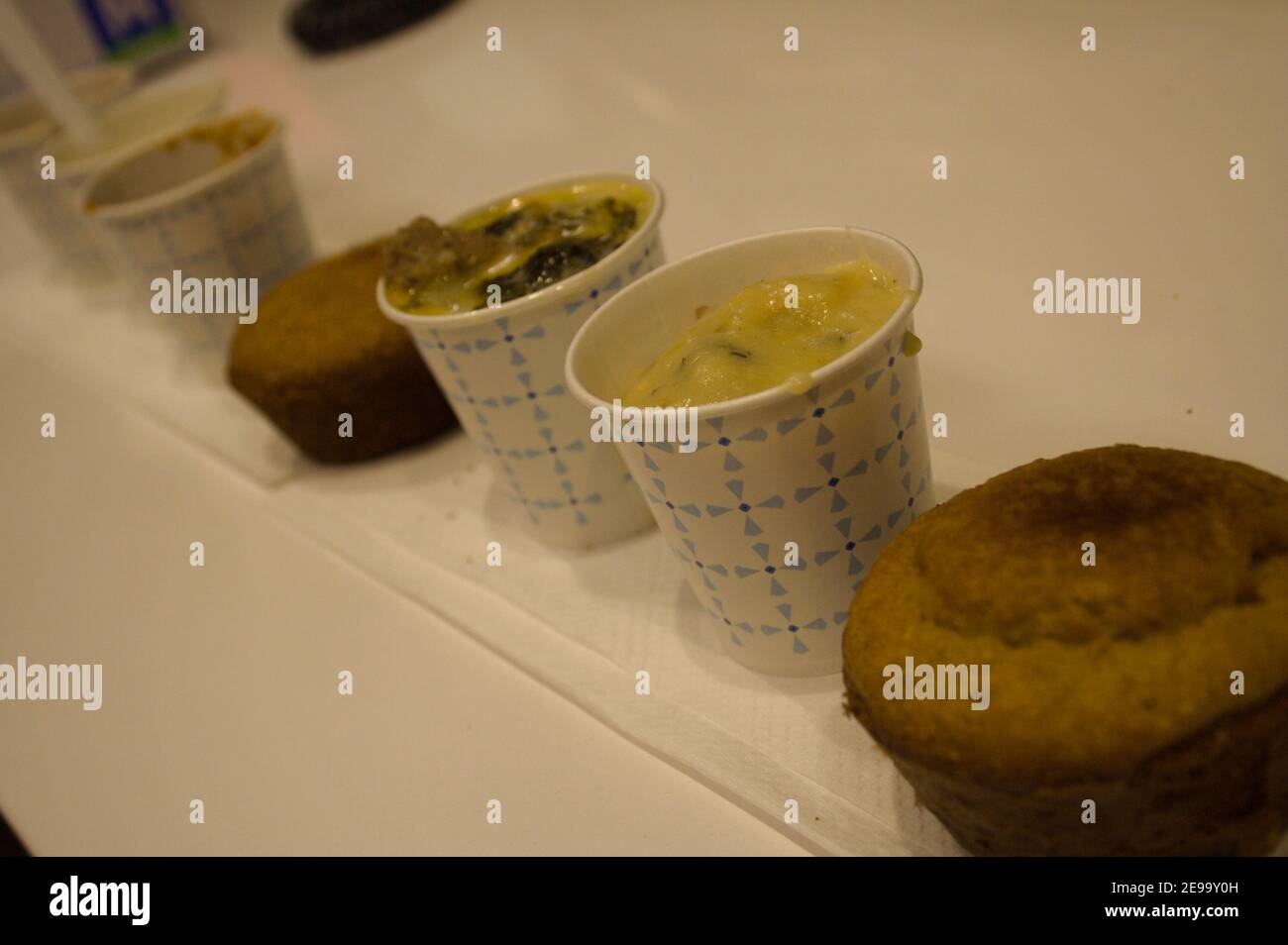 Una fila di piccoli assaggi di zuppe e muffin al cornbread su un ripiano bianco. Foto Stock