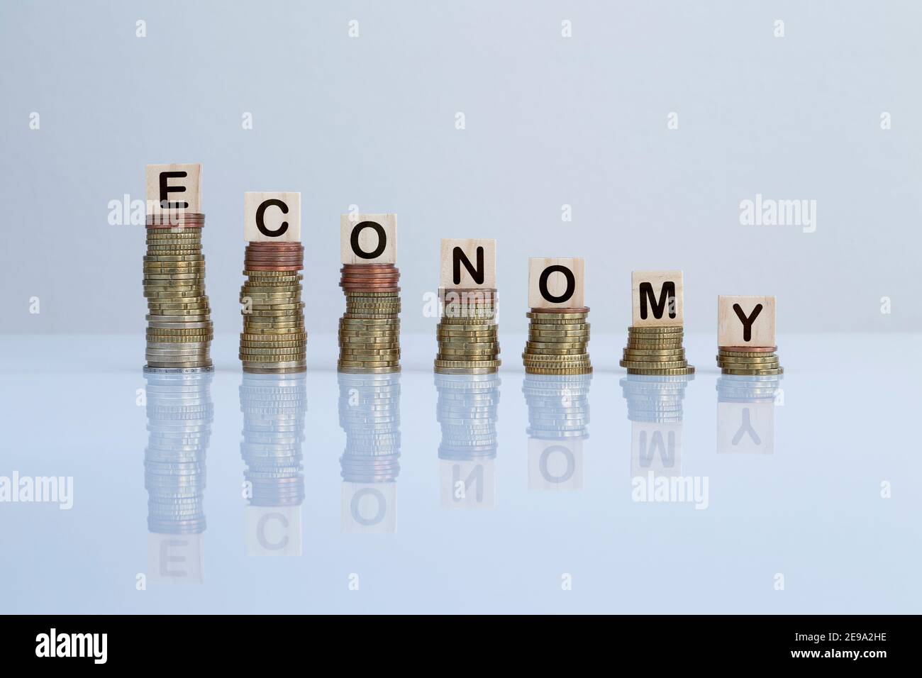 Parola 'ECONOMIA' su blocchi di legno in cima a pile discendenti di monete. Foto concettuale di crisi economica, recessione, riduzione finanziaria e fallimento. Foto Stock