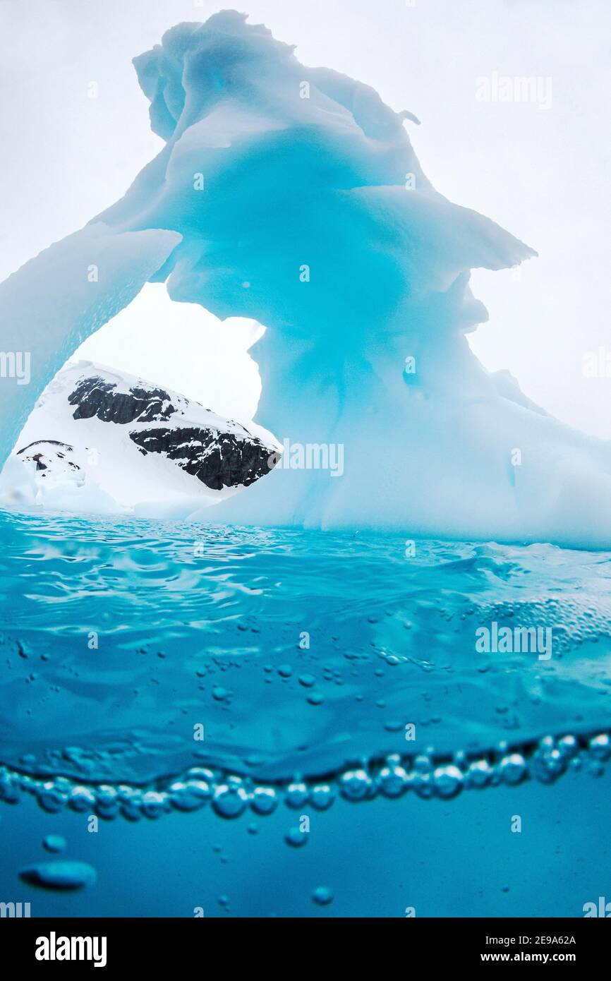 Vista sopra e sotto di un arco formato in un iceberg a Cuverville Island, canale di Ererra, Antartide. Foto Stock