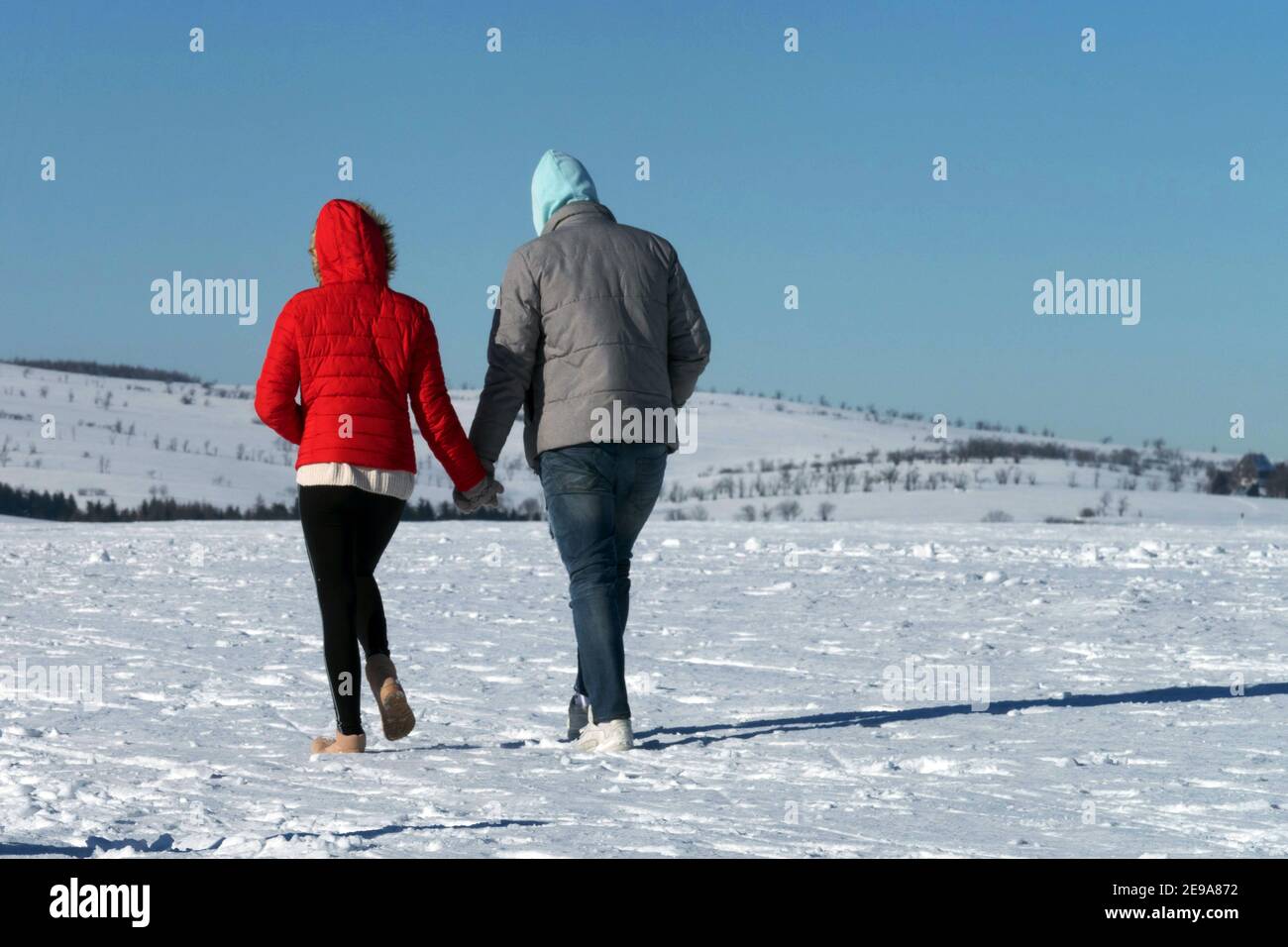 Uomo donna coppia che si allontana nella campagna invernale innevata e si tiene per mano, donna vista posteriore che cammina Foto Stock