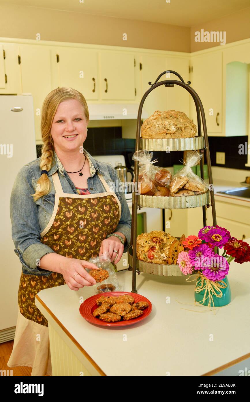 Un bel panettiere domestico caucasico adulto che mette i biscotti freschi fatti in casa in borsa, stativo di cottura con gli articoli sul banco della cucina, Wisconsin, USA Foto Stock