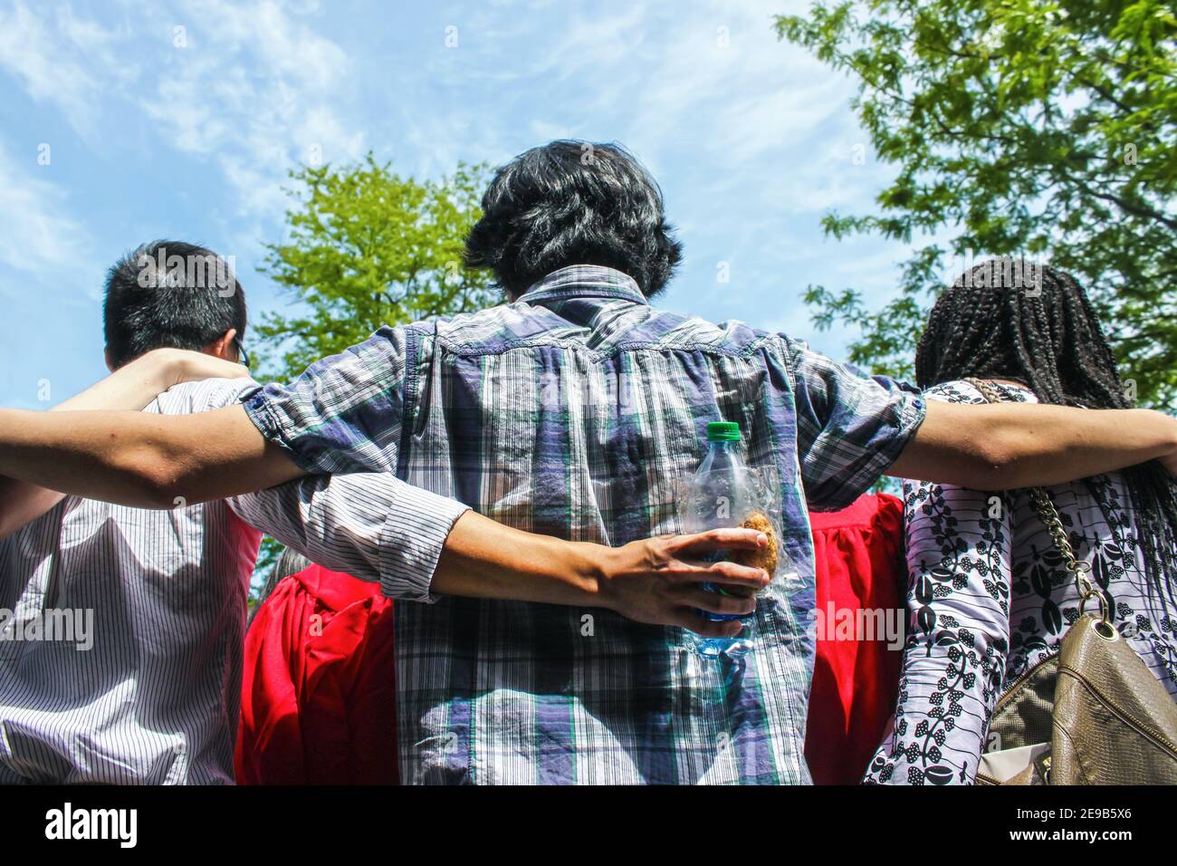 Amici dei laureati - vista posteriore del gruppo di amici multietnici con braccia intorno alle spalle - uno tenere spuntini - parlare con un laureato Foto Stock