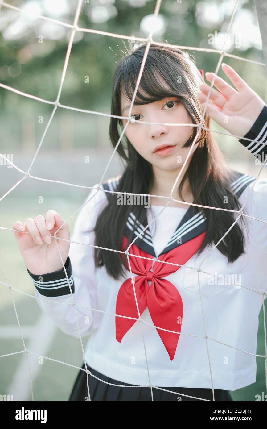 Ritratto dell'uniforme asiatica giapponese della ragazza della scuola superiore che osserva con reti di obiettivo di calcio Foto Stock