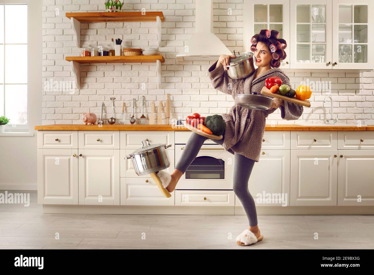 Casalinga stanca che porta un sacco di pentole pesanti, pentole e taglieri in cucina Foto Stock